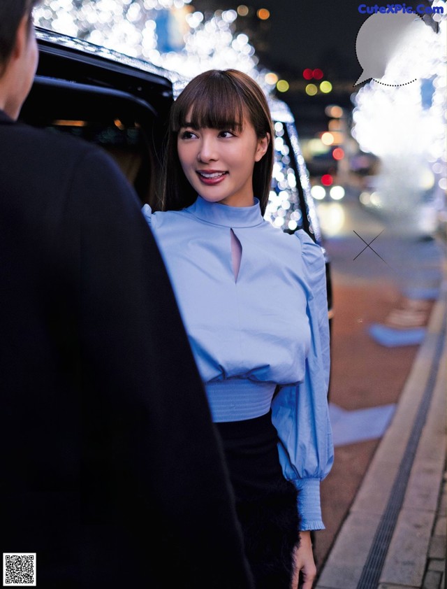 A woman in a blue shirt and black skirt standing next to a car.