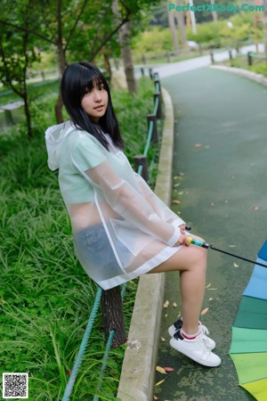 A woman sitting on a bench holding a rainbow colored umbrella.