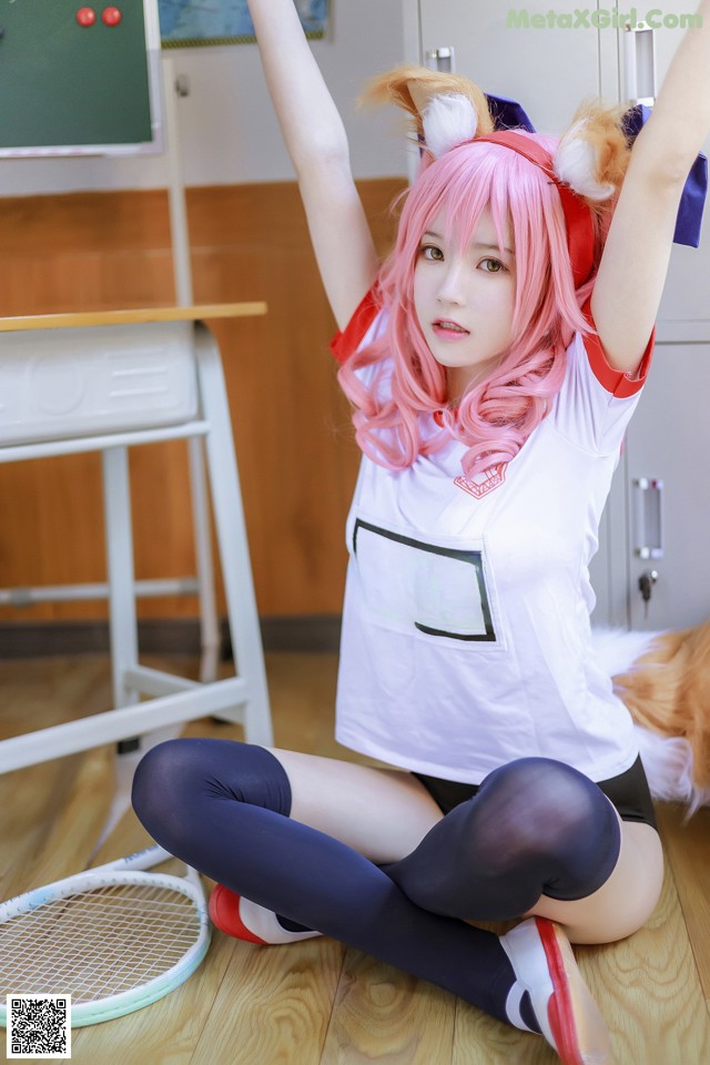 A woman with pink hair sitting on the floor with a tennis racket.