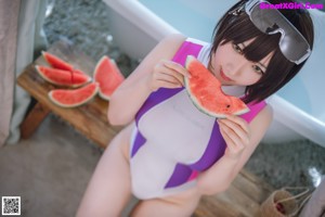 A woman in a bathing suit sitting on a table with a watermelon.