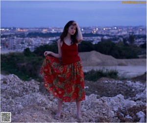 A woman in a red dress sitting on a rock.