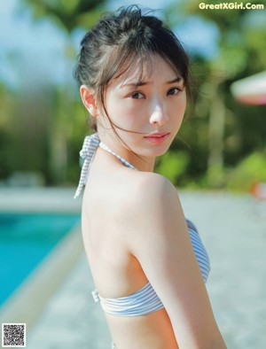 A woman in a bikini standing next to a swimming pool.