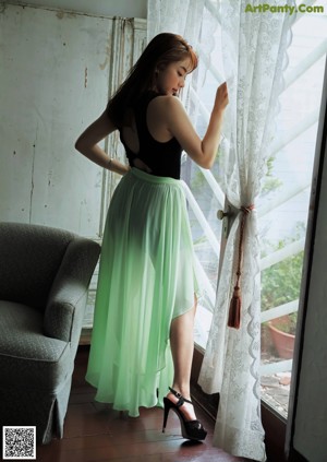 A woman in a long dress standing by a window.