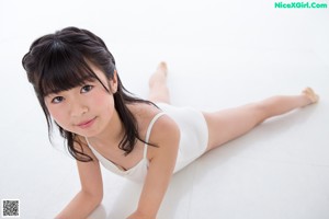 A woman in a white leotard leaning against a wall.