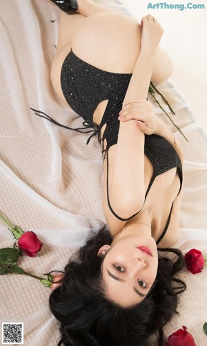 A woman in a black bodysuit laying on a bed with red roses.