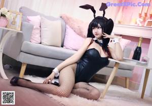 A woman in a black dress laying on a pink couch.