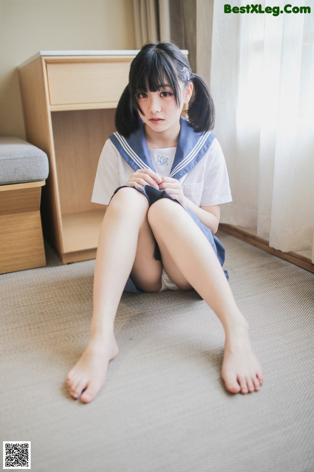 A woman in a school uniform sitting on the floor.