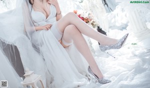 A woman in a white dress sitting on a white chair.