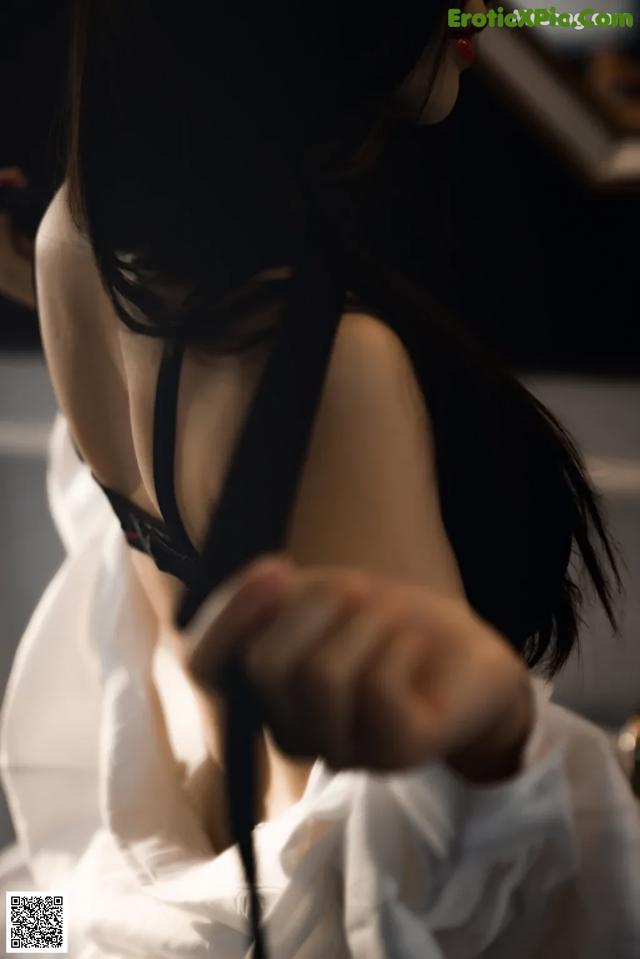 A woman in a white shirt is holding a black bra.