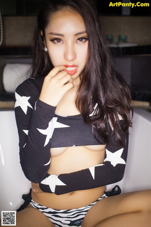 A woman in a black and white bikini sitting on a bathtub.