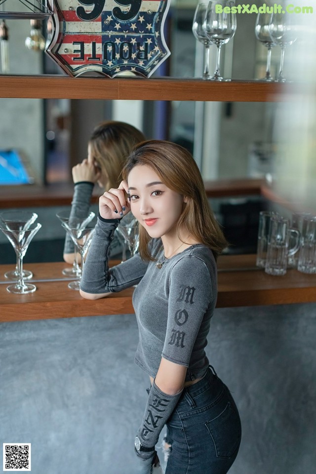 A woman standing in front of a bar holding a glass.