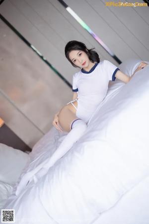 A woman in a white shirt and stockings sitting on a bed.