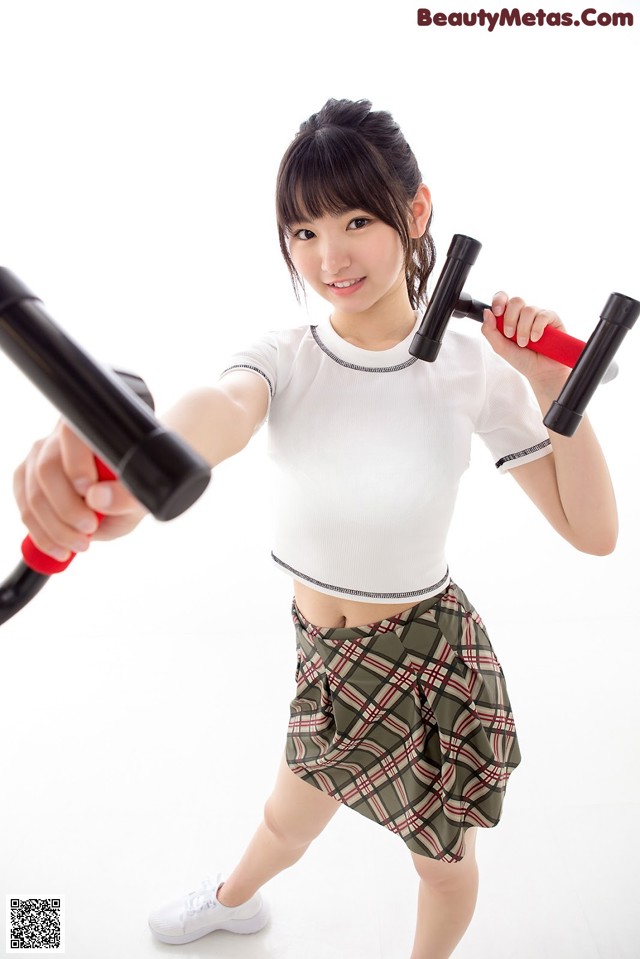 A woman in a white shirt and plaid skirt holding a pair of dumbbells.