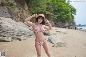 A woman in a bikini and a straw hat on a beach.