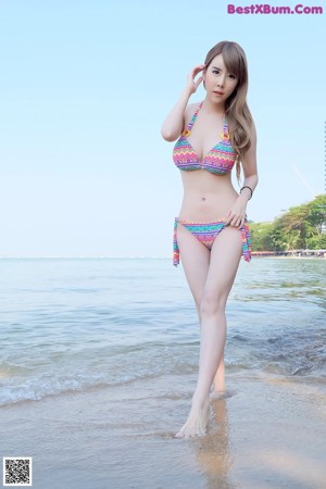 A woman in a bikini crouching down on the beach.