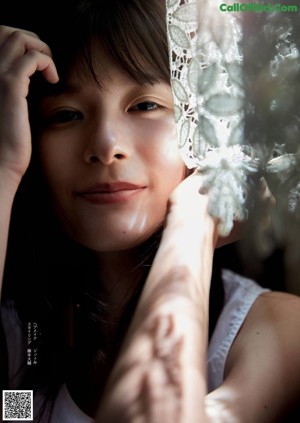 A woman in a white dress sitting by a window.