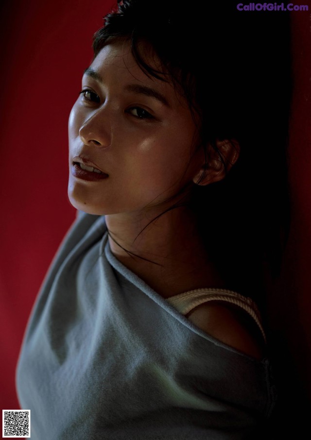 A woman in a gray shirt leaning against a red wall.