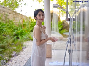 A woman in a white dress leaning against a pillar.