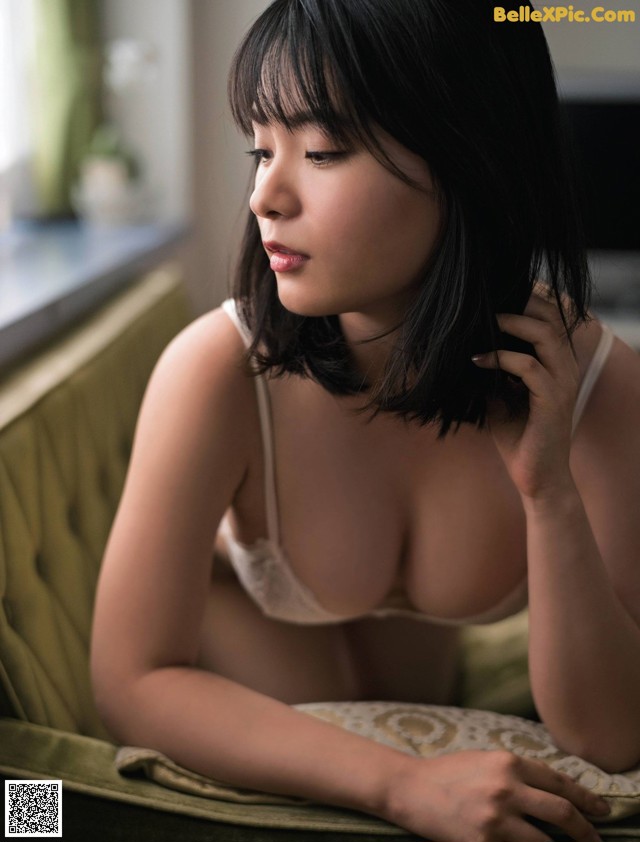 A woman in a white bra sitting on a green couch.