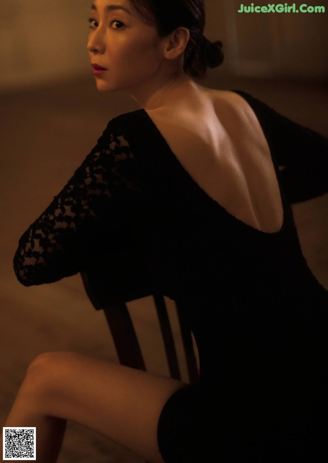 A woman in a black dress sitting on a chair.