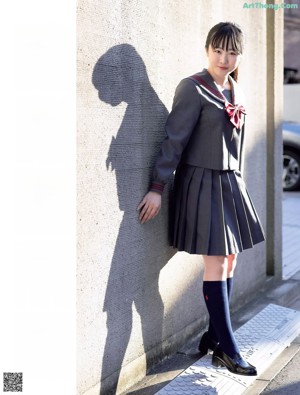 A young woman in a school uniform holding a blue bag.