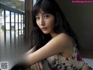 A woman sitting on top of a bed next to a window.