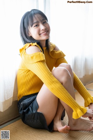 A woman in a yellow sweater sitting on a window sill.