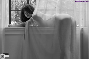 A woman in a white bodysuit leaning against a window.