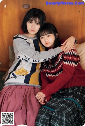 Two young women standing next to each other in front of a tree.