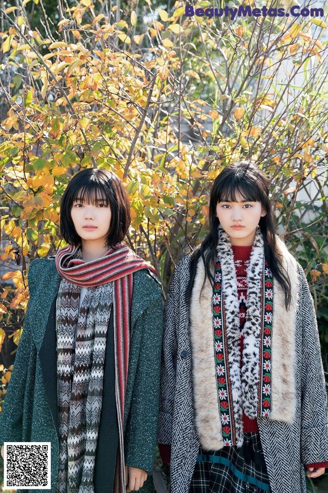 Two young women standing next to each other in front of a tree.