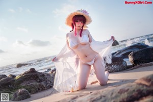 A woman in a bikini and straw hat standing in the water.