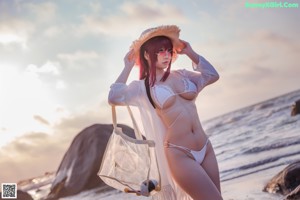 A woman in a bikini and hat sitting on a beach.