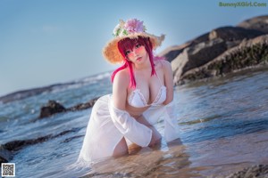 A woman with pink hair wearing a straw hat on the beach.