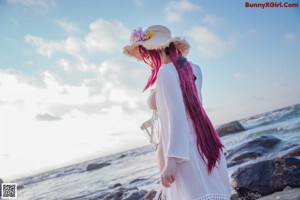 A woman in a white bikini and straw hat on the beach.