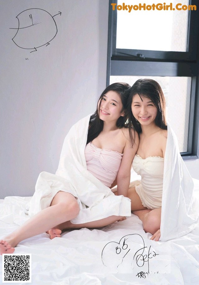 A couple of women sitting on top of a bed.