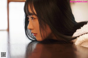 A young woman sitting on the floor in a white tank top.