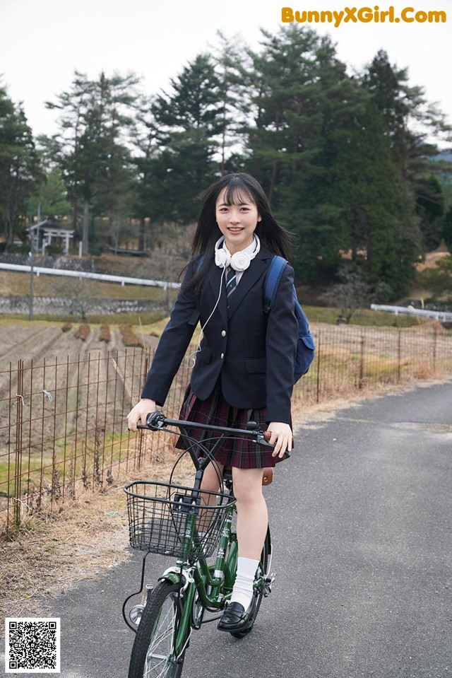 A woman in a school uniform riding a bike down a road.