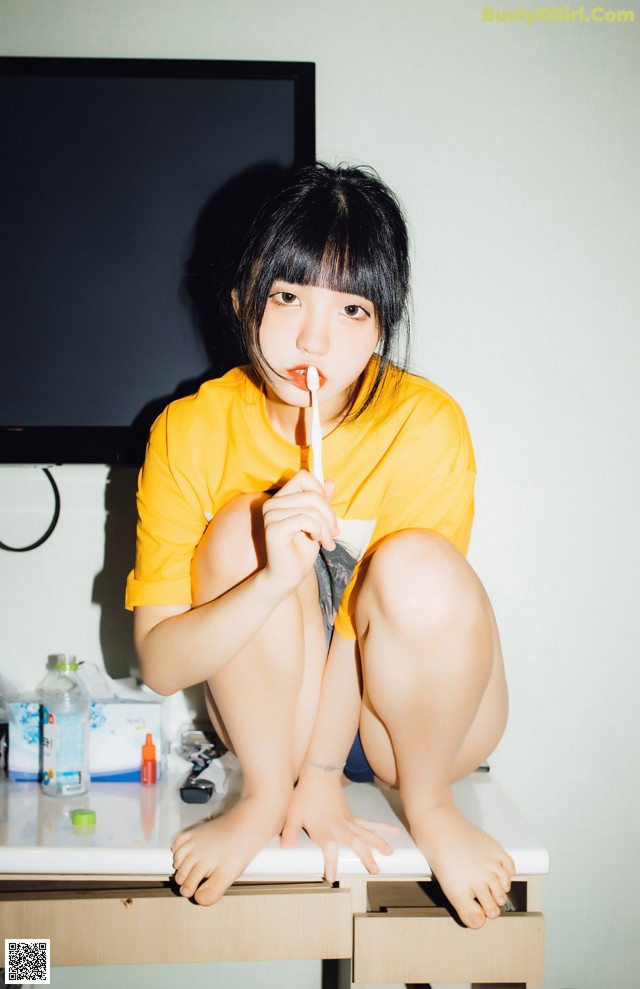 A woman sitting on top of a desk holding a toothbrush.