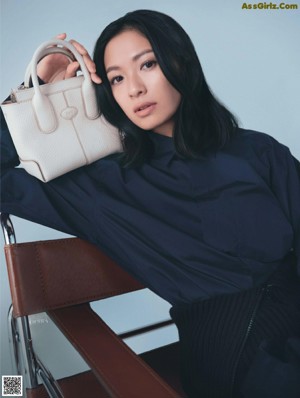 A woman sitting on a chair wearing a brown sweater and skirt.