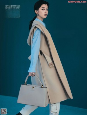 A woman standing in front of a window wearing a coat.