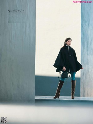 A woman standing in front of a window wearing a black coat.