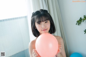 A woman in a bikini sitting on the floor with balloons.