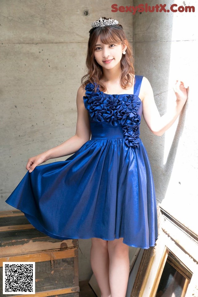 A woman in a blue dress leaning against a wall.