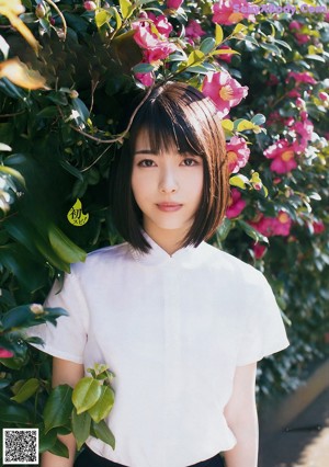 A woman in a white shirt and a blue hat standing next to a tree.