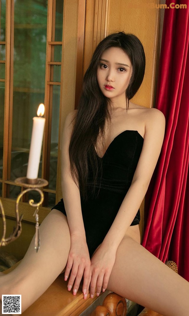 A woman in a black bodysuit sitting on a chair next to a candle.