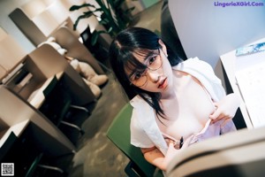 A woman sitting on top of a desk next to a book shelf.